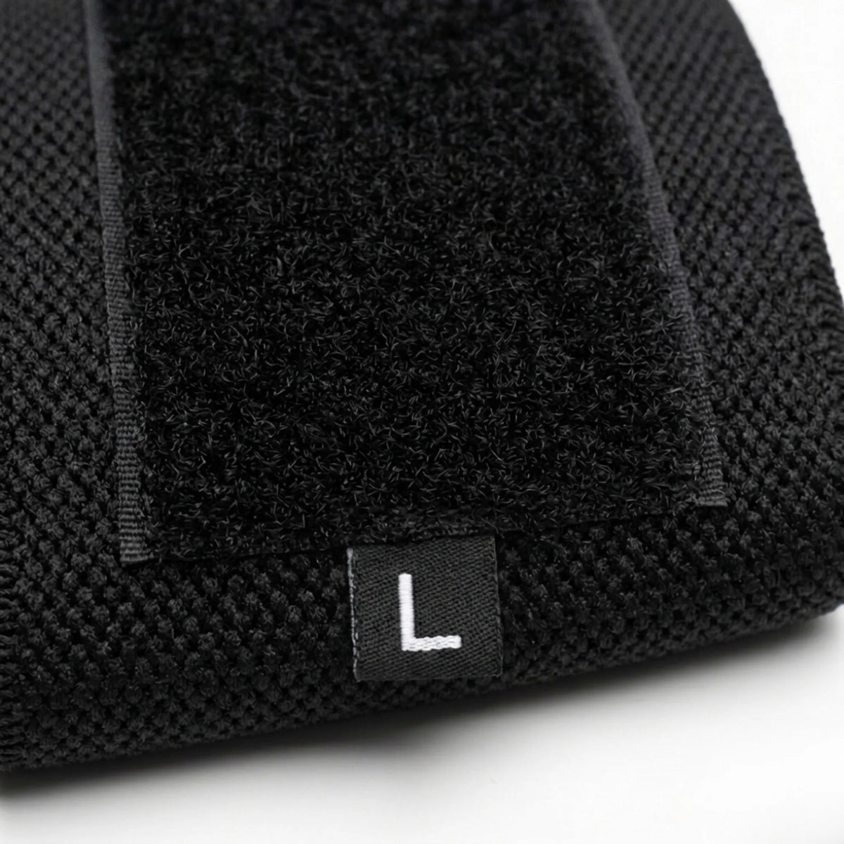 Detalhe da faixa de pulso preta mostrando o fechamento em velcro, a textura do tecido e a etiqueta L